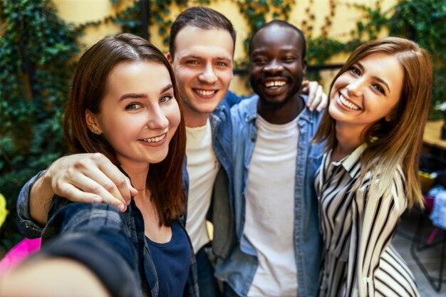 Deux filles et deux garçons prennent une photo de selfie à l'extérieur, se serrant dans leurs bras et avec un sourire sincère