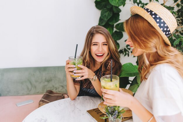 Deux filles joyeuses partageant des potins après le travail et en riant, tout en se détendant dans un café élégant