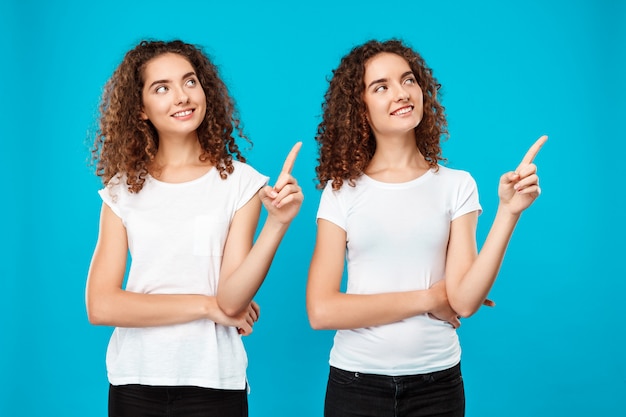 Deux filles jumelles souriant, pointant du doigt sur le mur bleu