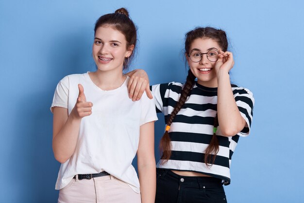 Deux filles ont l'air heureux, pointant et regardant avec une expression positive, mesdames debout dans des vêtements élégants isolés.