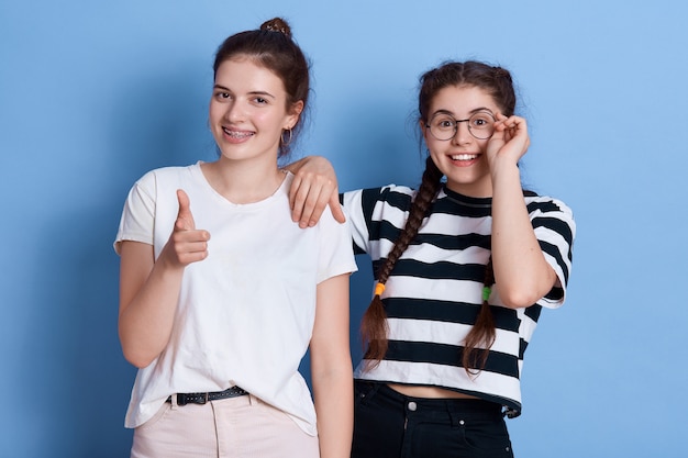 Deux filles ont l'air heureux, pointant et regardant avec une expression positive, mesdames debout dans des vêtements élégants isolés.