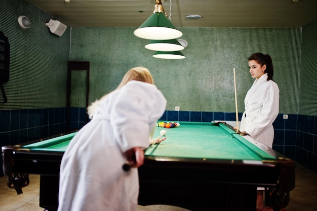 Deux filles sexy en peignoir blanc jouent au billard