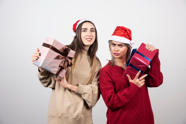 Deux filles souriantes en bonnet de Noel tenant des cadeaux de Noël festifs.