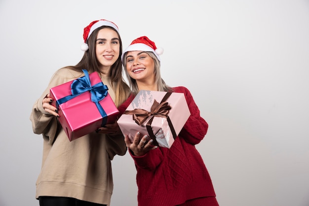 Deux filles souriantes en bonnet de Noel tenant des cadeaux de Noël festifs.