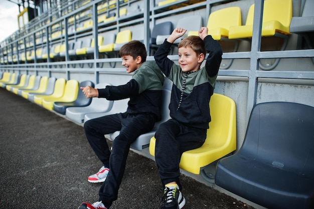 Photo gratuite deux frères soutiennent leur équipe favorite assis sur le podium sportif du stade