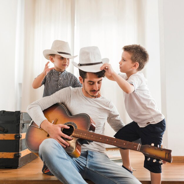 Deux garçons jouant avec leur père tenant une guitare