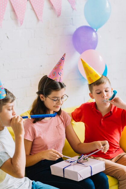 Deux garçons sonnant la corne pendant que leur ami déballe un cadeau d&#39;anniversaire