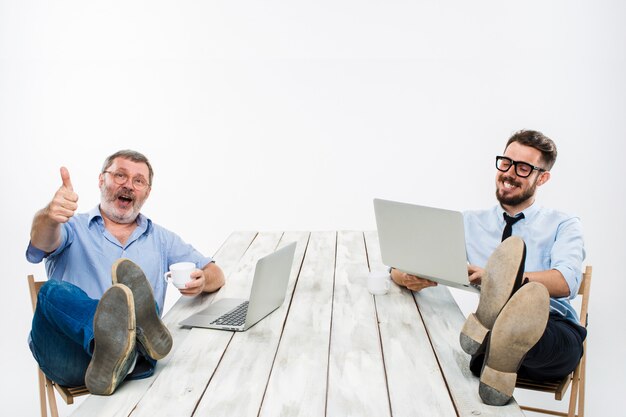 Les deux hommes d'affaires avec les jambes sur la table travaillant sur des ordinateurs portables