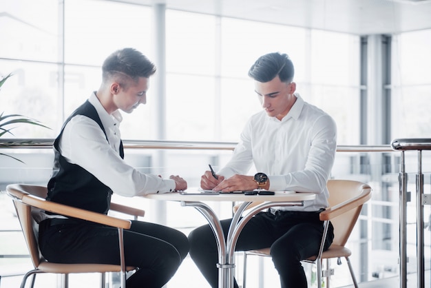 Deux hommes d'affaires signent des documents dans un grand bureau spacieux