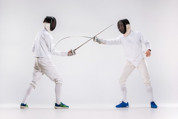 Les deux hommes portant un costume d'escrime pratiquant avec l'épée contre le gris