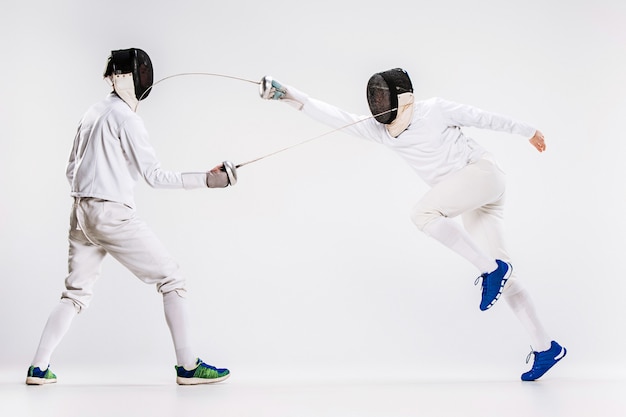 Les deux hommes portant un costume d'escrime pratiquant avec l'épée contre le gris