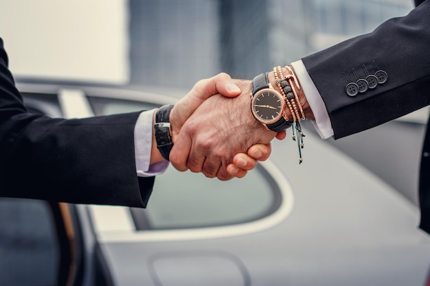 Photo gratuite deux hommes se serrent la main devant la voiture.