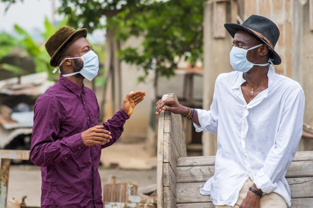 Deux jeunes amis afro-américains portant des masques protecteurs riant et distanciant socialement