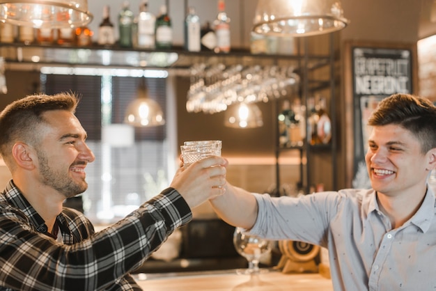 Photo gratuite deux jeunes amis souriants soulevant des toasts au bar