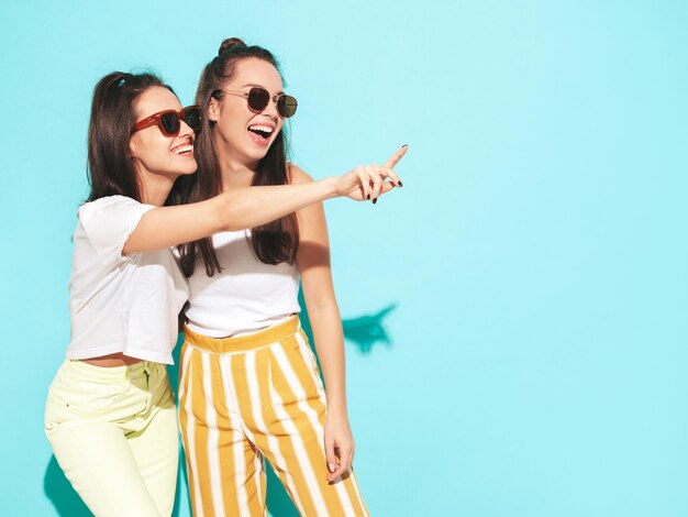 Deux jeunes belles femmes hipster blondes souriantes dans des vêtements d'été à la mode Sexy femmes insouciantes posant en studio Modèles positifs s'amusant Gai et heureux