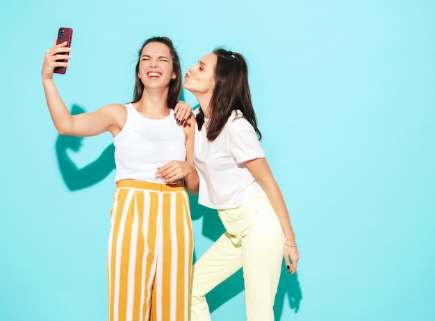 Deux jeunes belles femmes hipster blondes souriantes dans des vêtements d'été à la mode Sexy femmes insouciantes posant en studio Modèles positifs s'amusant Gai et heureux