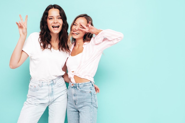 Deux jeunes belles femmes hipster brune souriante dans des vêtements d'été à la mode Sexy femmes insouciantes posant près du mur bleu Modèles positifs s'amusant Enthousiaste et heureux