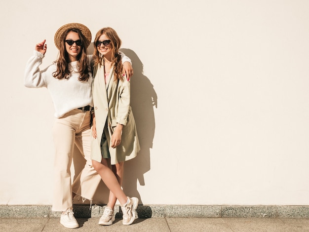 Deux jeunes belles femmes hipster souriantes en pull et manteau blancs à la mode