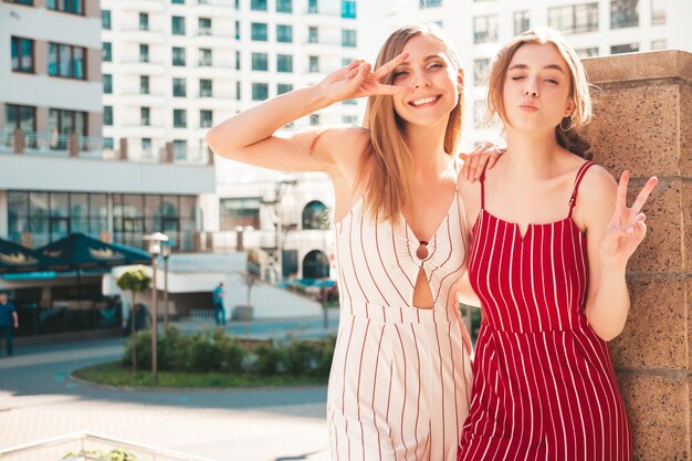 Deux jeunes belles femmes hipster souriantes en salopette à la modeFemmes insouciantes sexy posant sur le fond de la rue Modèles positifs s'amusant à s'étreindre et à devenir fous