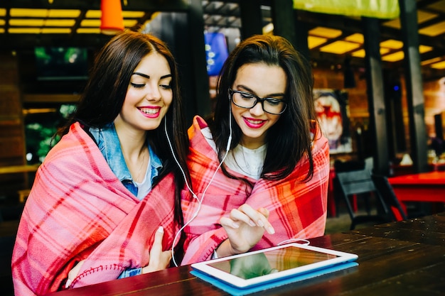 Deux jeunes et belles filles assises à la table regardant quelque chose sur une tablette