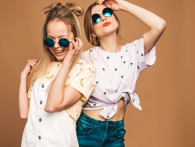 Deux jeunes belles filles blondes blondes souriantes dans des vêtements de T-shirt coloré d'été à la mode. et montrant la langue