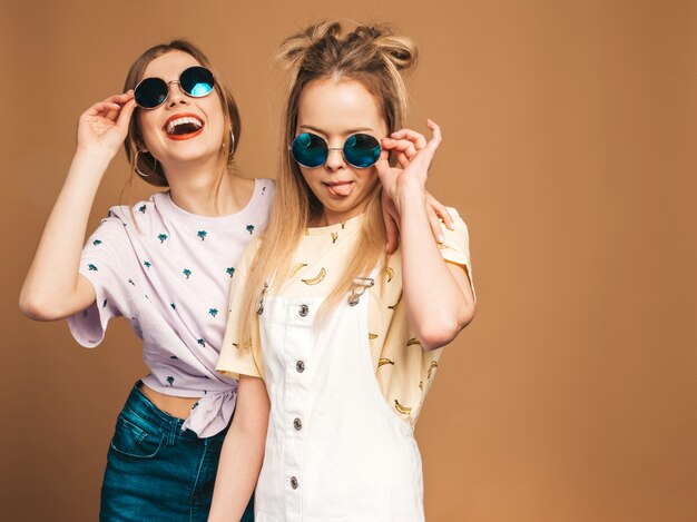 Deux jeunes belles filles blondes blondes souriantes dans des vêtements de T-shirt coloré d'été à la mode.