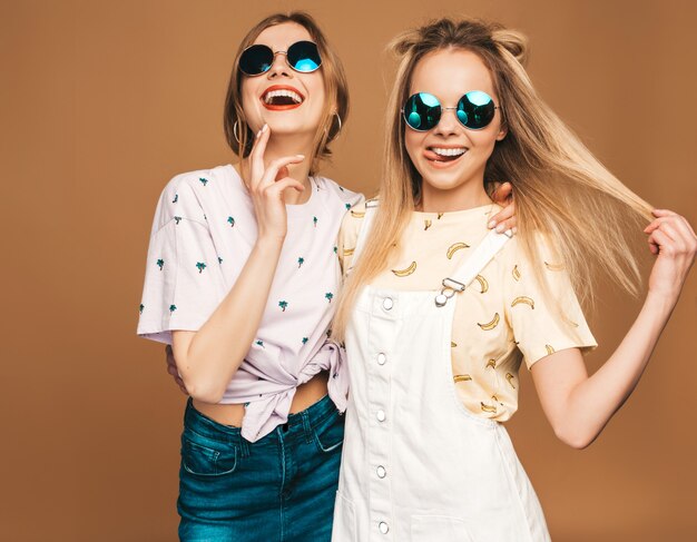 Deux jeunes belles filles blondes blondes souriantes dans des vêtements de T-shirt coloré d'été à la mode.