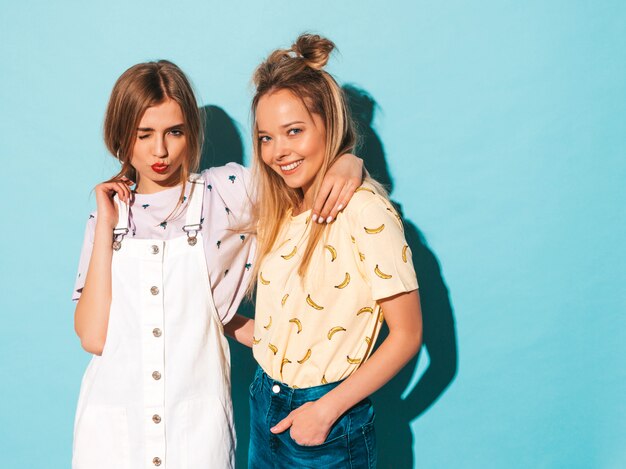 Deux jeunes belles filles blondes blondes souriantes dans des vêtements de T-shirt coloré d'été à la mode.