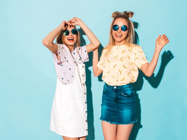 Deux jeunes belles filles blondes blondes souriantes dans des vêtements de T-shirt coloré d'été à la mode.