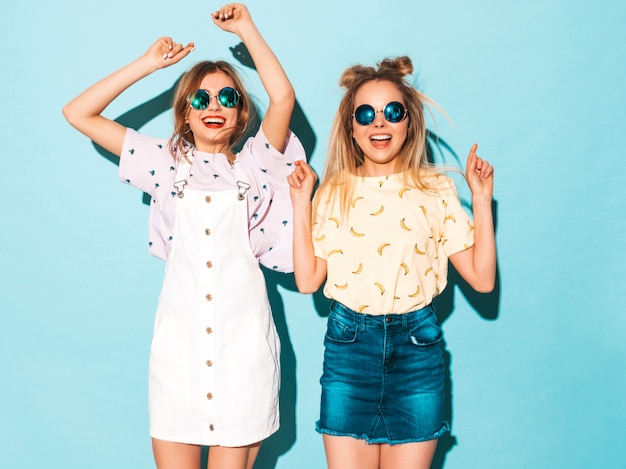 Deux jeunes belles filles blondes blondes souriantes dans des vêtements de T-shirt coloré d'été à la mode.