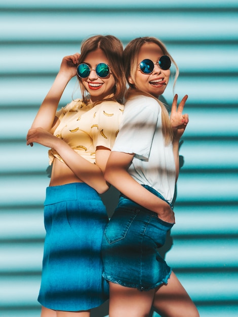 Deux jeunes belles filles blondes blondes souriantes dans des vêtements de T-shirt coloré d'été à la mode.