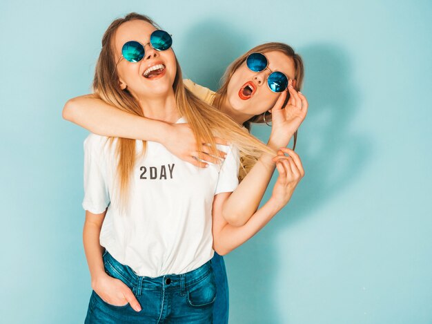 Deux jeunes belles filles blondes blondes souriantes dans des vêtements de T-shirt coloré d'été à la mode.