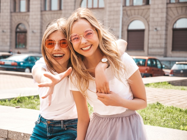 Deux jeunes belles filles blondes souriantes hipster en vêtements de t-shirt blanc à la mode d'été.