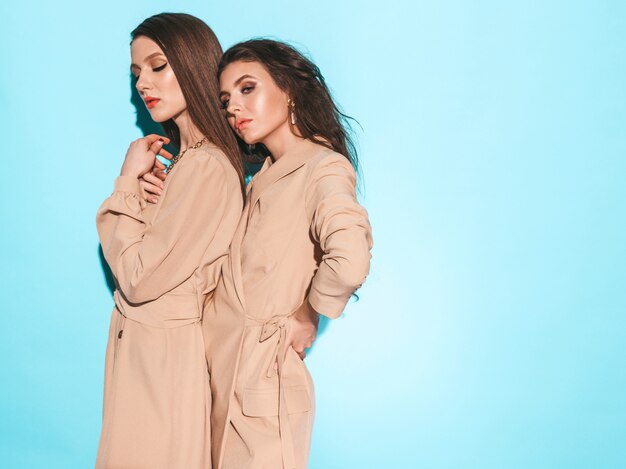 Deux jeunes belles filles brunes dans de beaux vêtements d'été à la mode.Des femmes insouciantes sexy posant près du mur bleu en studio