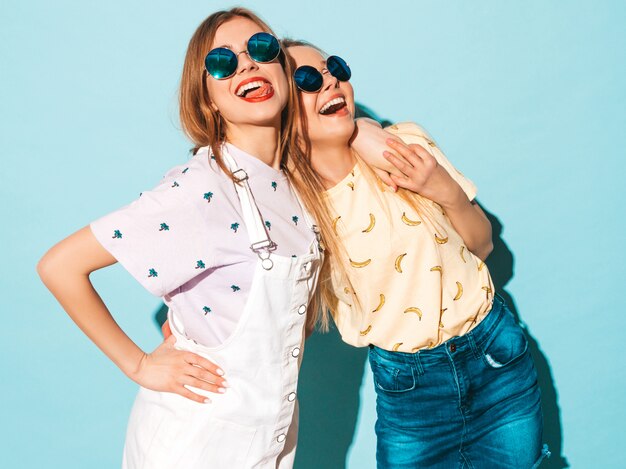 Deux jeunes belles filles hipster blondes souriantes en jeans d'été à la mode jupent les vêtements.