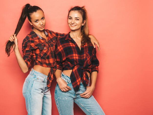 Deux jeunes belles filles hipster brune souriante dans une chemise à carreaux similaire à la mode et des vêtements en jeans.Des femmes insouciantes sexy posant près du mur rose en studio.Des modèles positifs s'amusant