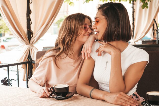 Deux jeunes belles filles hipster souriantes dans des vêtements décontractés d'été à la mode.Des femmes sans soucis discutant dans la terrasse d'un café terrasse et buvant du café.Des modèles positifs s'amusent et communiquent