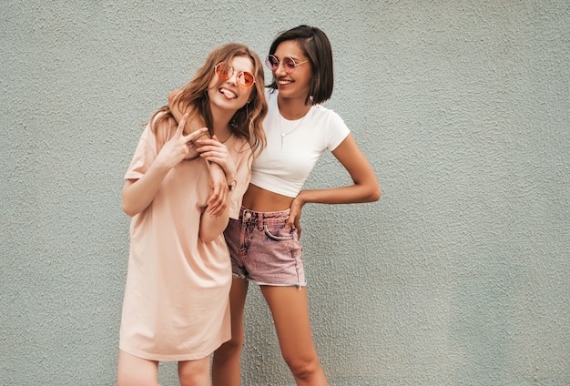 Deux jeunes belles filles hipster souriantes dans des vêtements d'été à la mode. Femmes insouciantes sexy posant sur fond de rue dans des lunettes de soleil. Modèles positifs s'amusant et étreignant