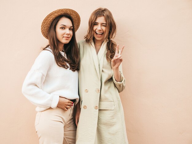 Deux jeunes belles filles hipster souriantes en pull et manteau blancs à la mode