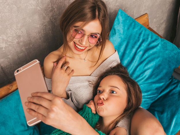 Deux jeunes belles filles magnifiques souriantes dans des vêtements d'été à la mode. Femmes insouciantes sexy posant à l'intérieur et prenant selfie. Modèles positifs s'amusant avec smartphone.