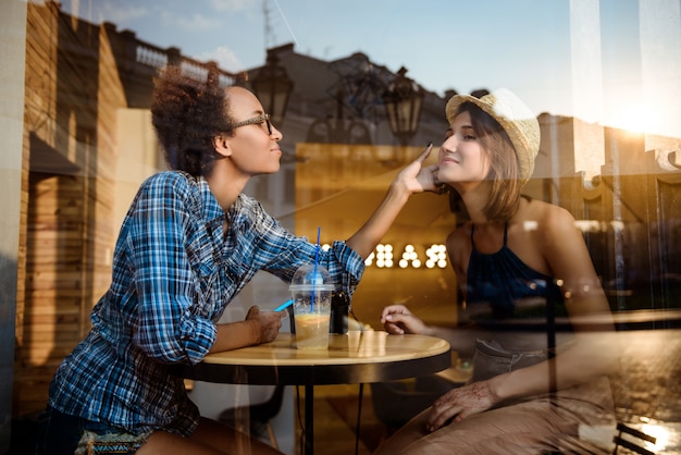 Photo gratuite deux jeunes belles filles souriant, parlant, se reposant au café. tiré de l'extérieur.