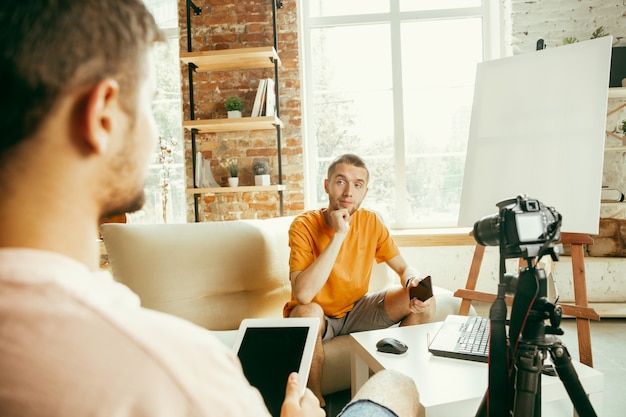 Deux jeunes blogueurs masculins de race blanche dans des vêtements décontractés avec un équipement professionnel ou une caméra d'enregistrement vidéo interview à la maison