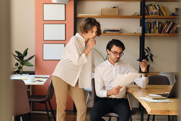 Deux jeunes collègues de travail travaillant attentivement avec des papiers dans un bureau moderne