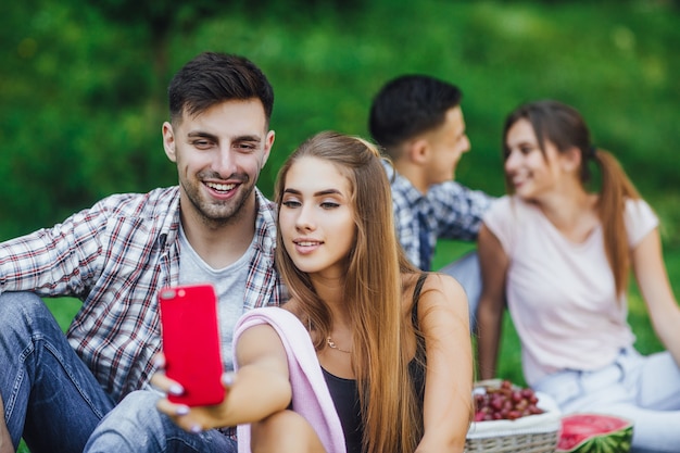 Deux jeunes couples heureux s'asseyant dans l'herbe au beau parc, ils ont un pique-nique