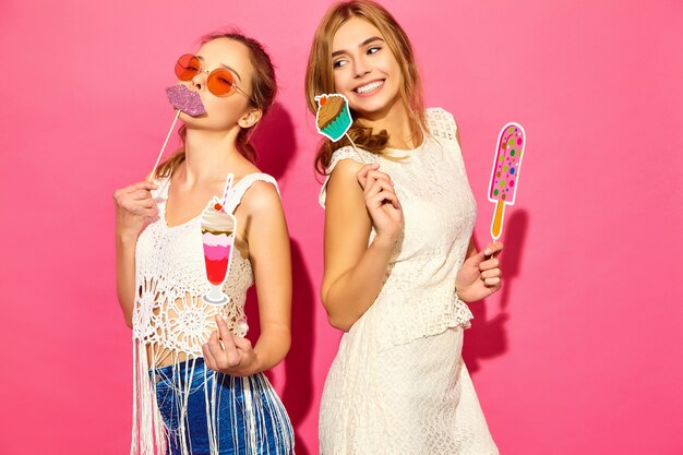 Deux jeunes femmes blondes souriantes élégantes mangeant des accessoires de crème glacée sucrée et de faux cocktails.