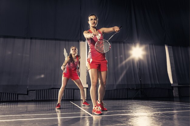 Les deux jeunes femmes jouent au badminton sur une salle de sport. jeu de concept par paire