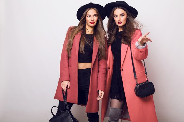 Deux jeunes femmes à la mode en manteau de printemps à la mode décontractée, des bottes à talons, un chapeau noir et un sac à main élégant