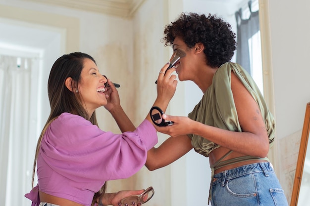 Deux jeunes femmes s'amusant à se maquiller. Les filles s'amusent avant d'enregistrer une vidéo sur le maquillage en appliquant du rouge avec des pinceaux sur les joues et en riant. Cosmétiques, beauté, concept de blogs