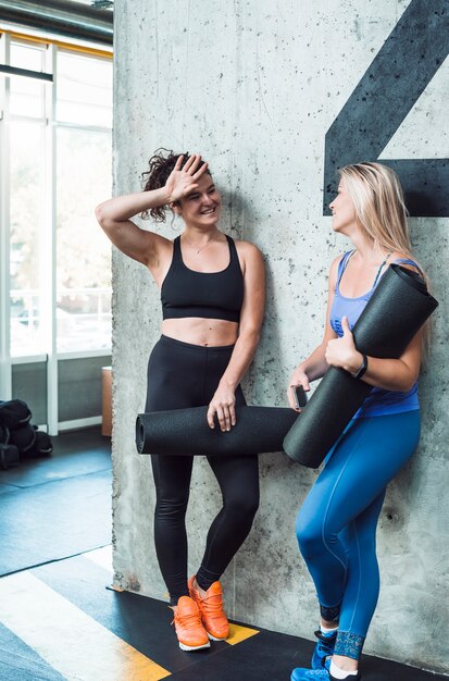 Deux jeunes femmes souriantes avec tapis d&#39;exercice dans la salle de gym