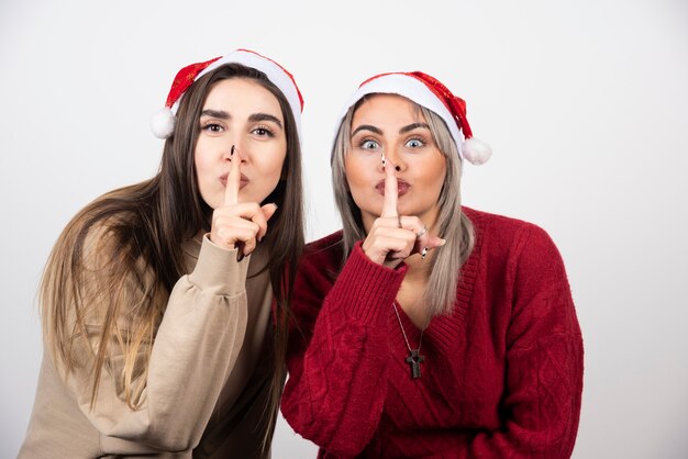 Deux jeunes filles en bonnet de Noel faisant signe silencieux.